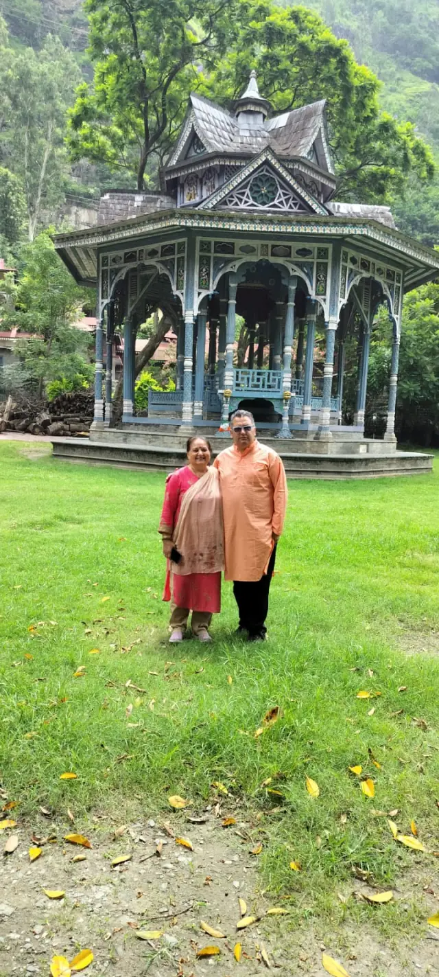 Couple standing on a lawn in front of a carved heritage pavilion in Himachal